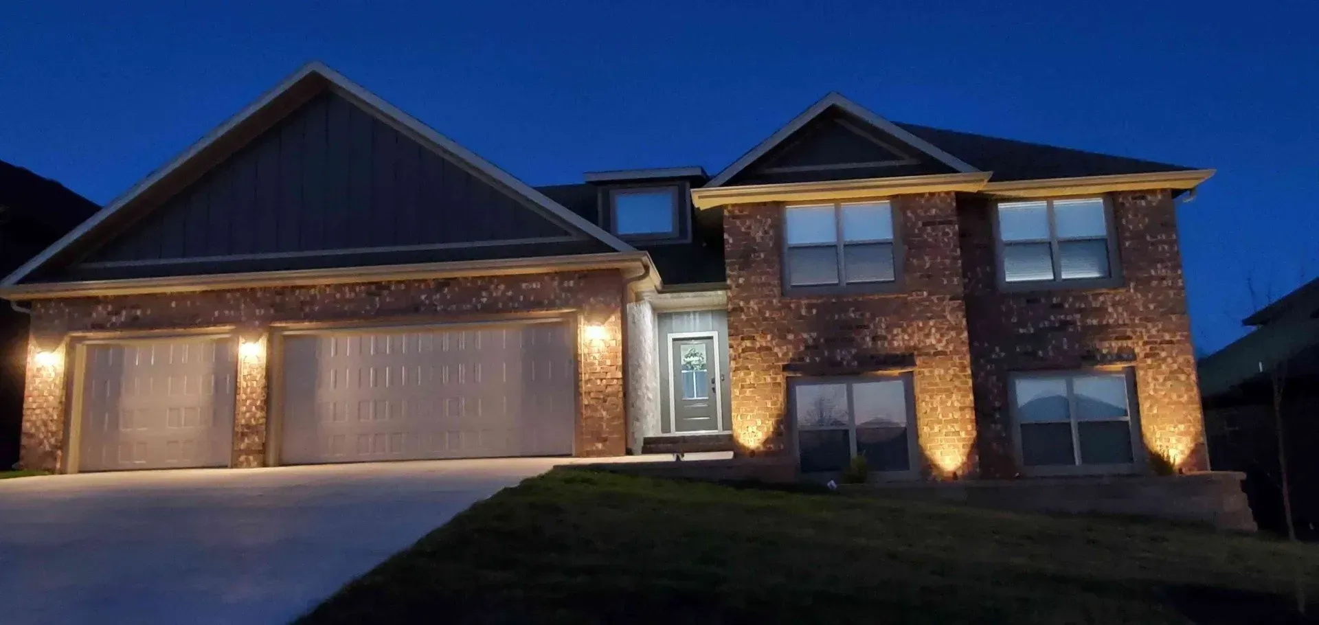 A house at night, lit by a lamp. A grass lawn is in the foreground.