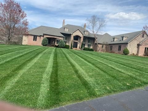 Green striped lawn in front of a large brick house under a blue sky.