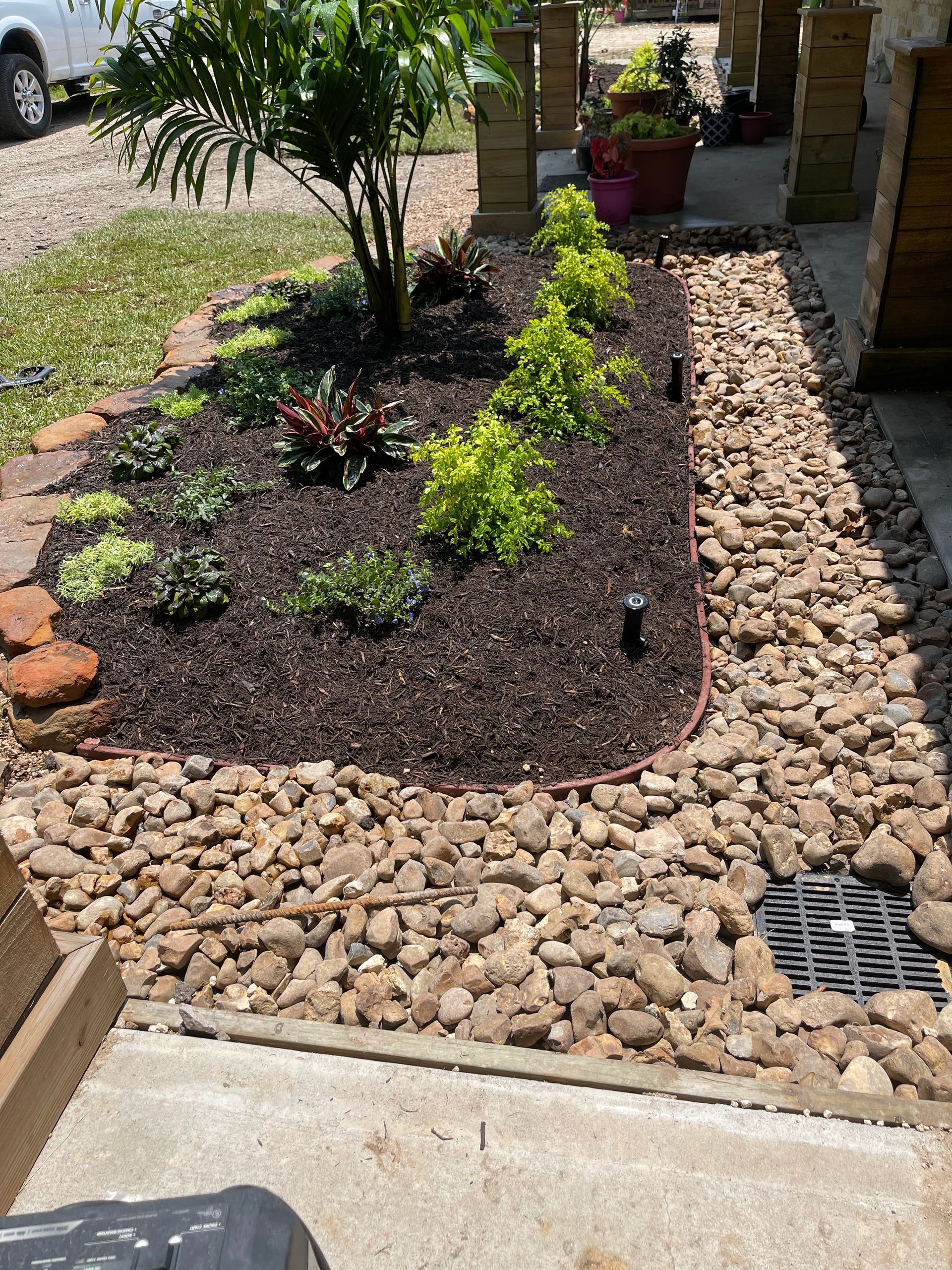 Flower bed with red flowers, edged with stone, near a parking lot.