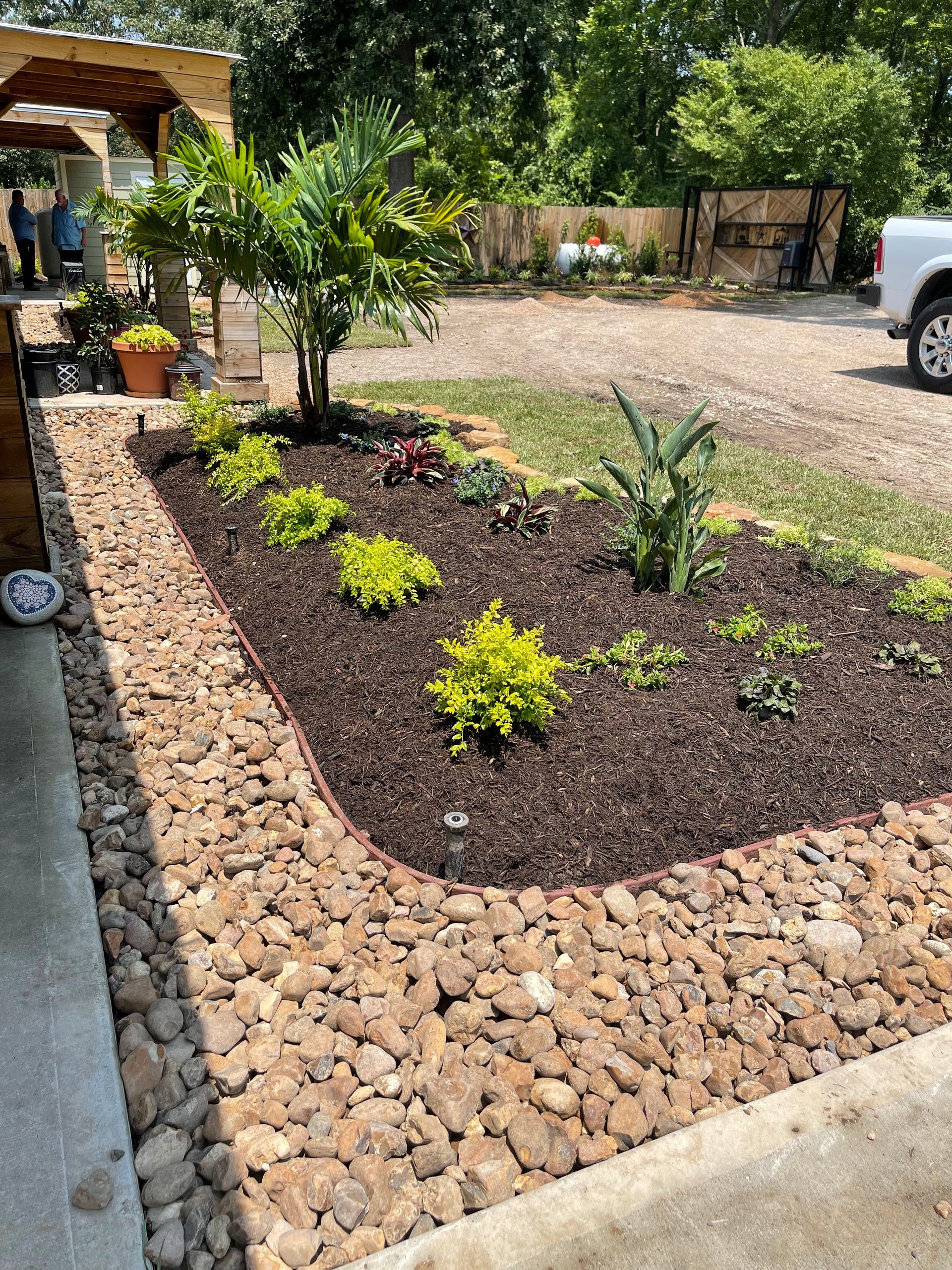 Flower bed with black mulch and brick edging, various colorful flowers, and green plants.