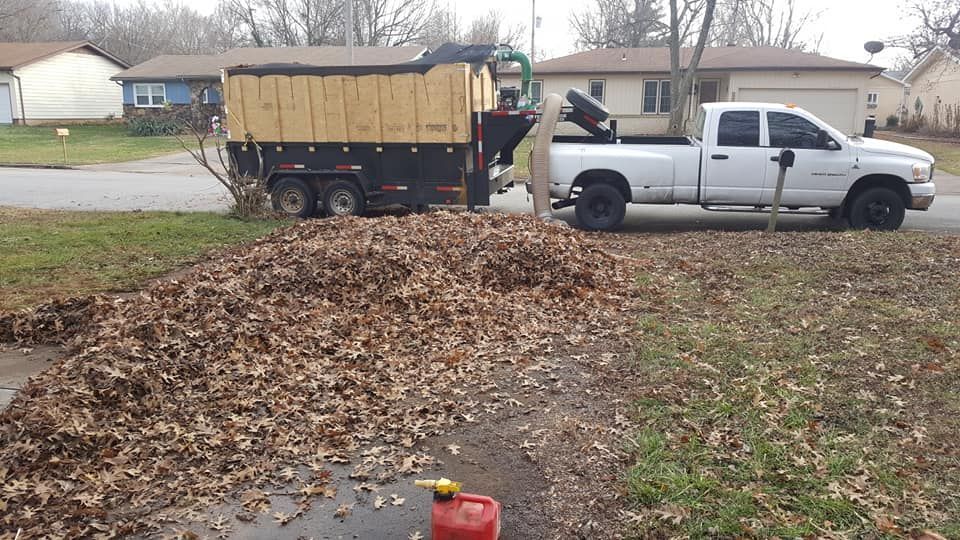 Truck with leaf vacuum loading trailer full of leaves in a residential driveway.