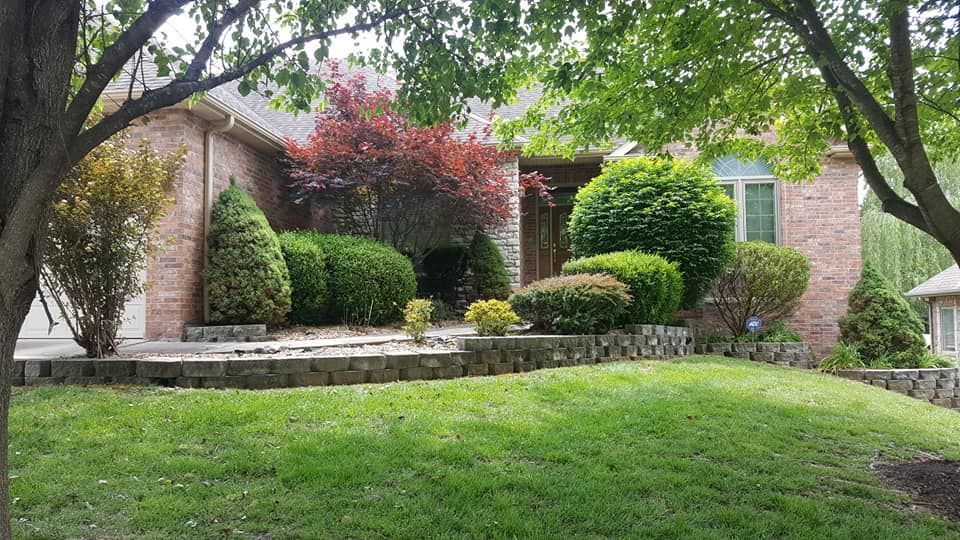 A brick house with well-maintained landscaping, including green bushes, and trees with lush foliage.