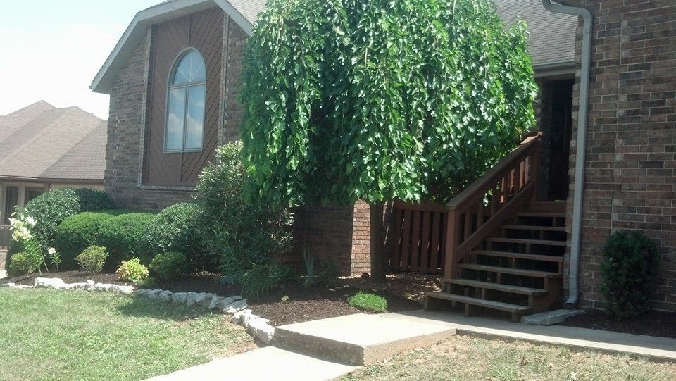 House exterior with brick siding, wooden stairs, and a large tree in front.