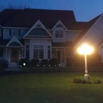 A house at night, lit by a lamp. A grass lawn is in the foreground.