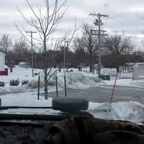 Snowy scene through a window. Bare trees, power lines, and a tire in the foreground; snow on the ground.