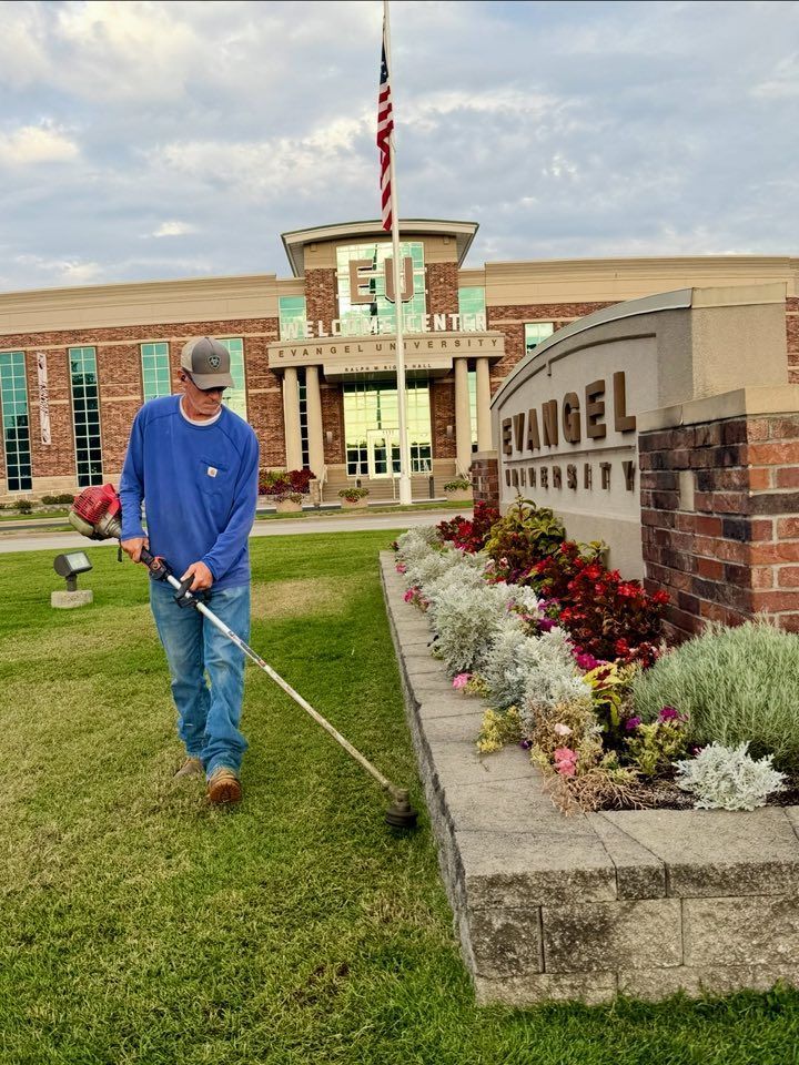 Man on a yellow riding lawnmower mowing grass in a grassy field with trees in the background.