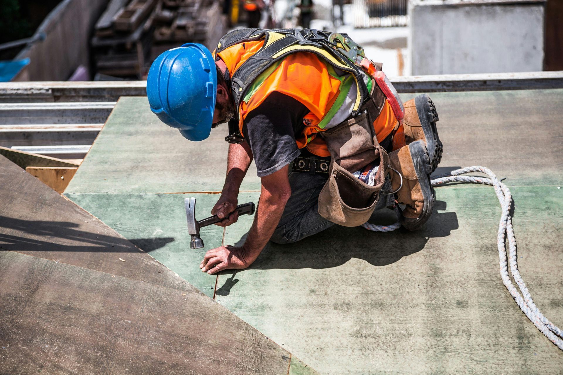 Construction worker hammering on a rooftop, wearing safety gear and a blue hard hat.