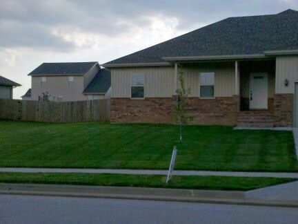 Suburban house with brick facade, green lawn, and cloudy sky.