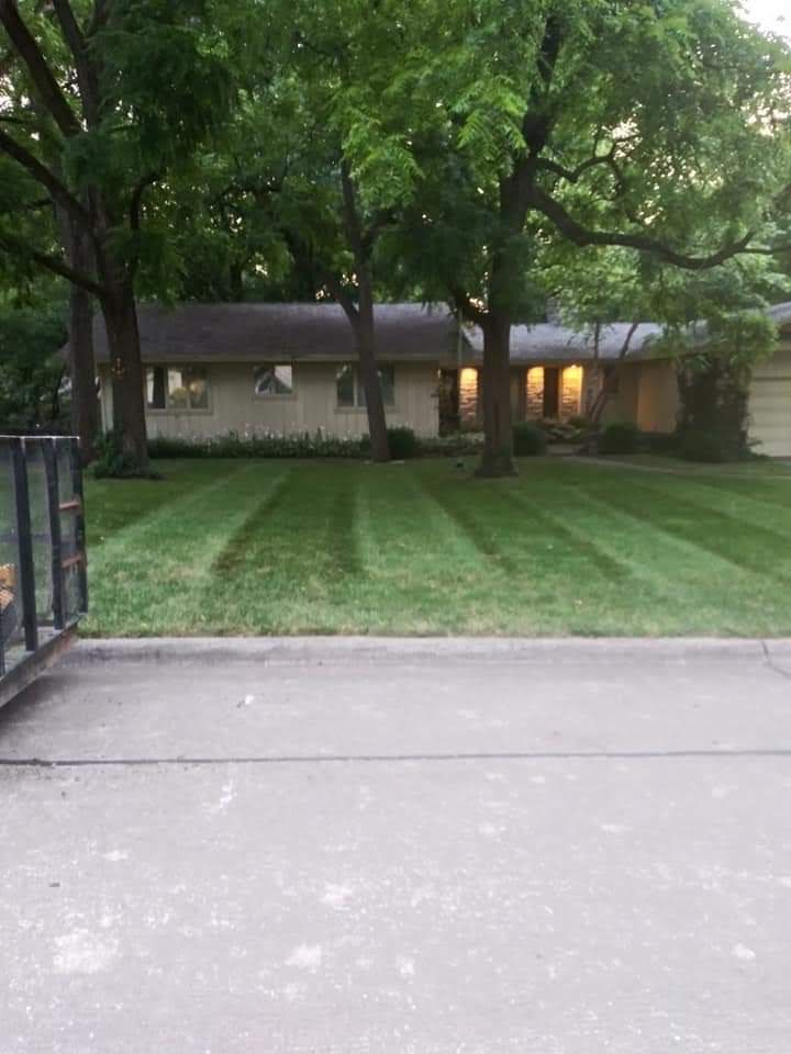 A house with freshly mowed green lawn. Trees frame the building. Gray concrete in foreground.