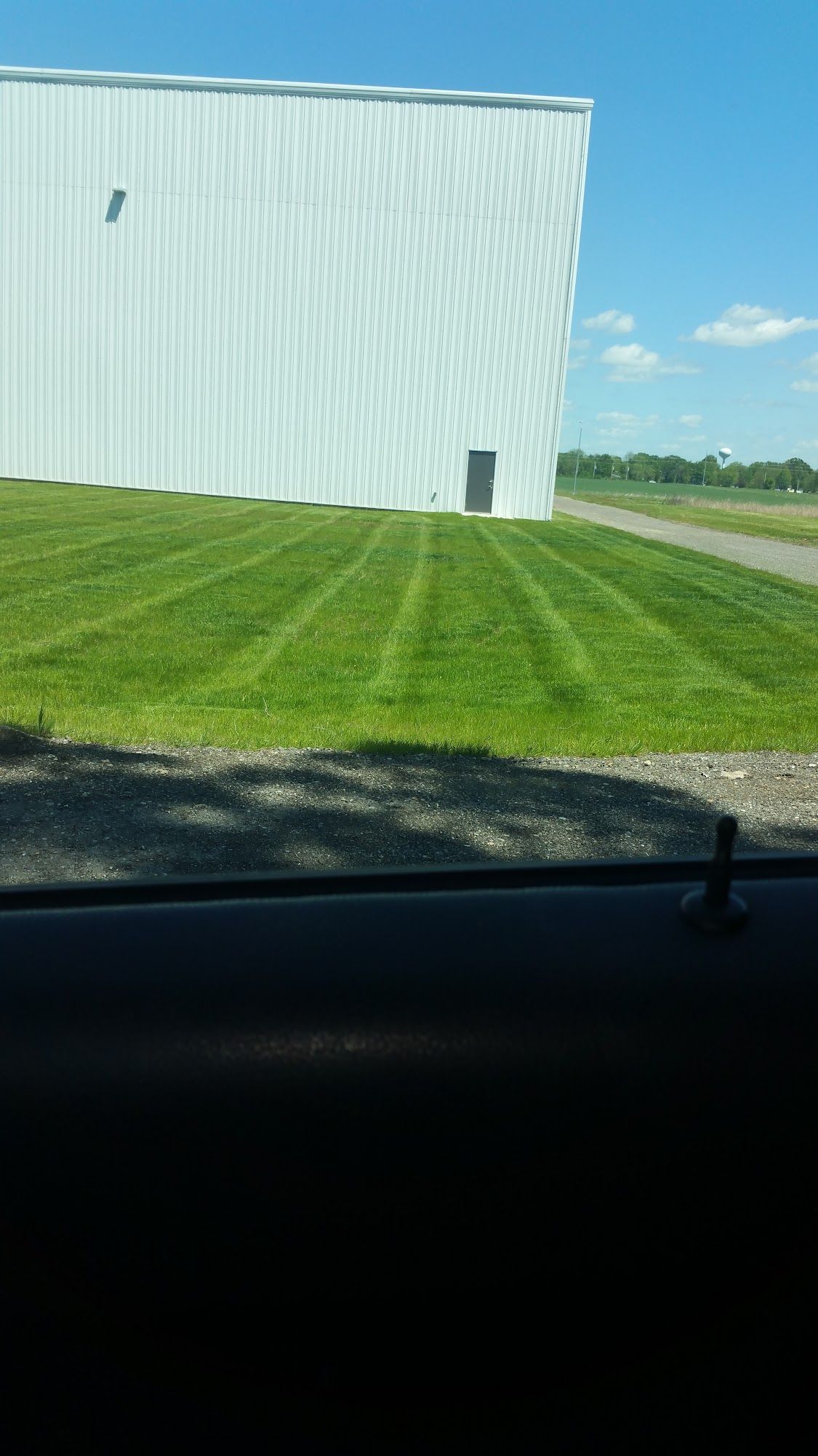 Green lawn with striped mowing pattern, large white building in background, blue sky.