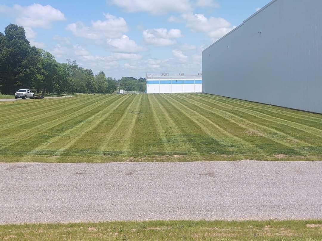 Lawn mowed in stripes next to a large white building under a blue sky with clouds. A car is visible on the left.