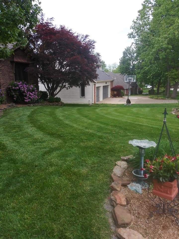 Lawn with striped pattern, a bird bath, and a red-leafed tree in front of a brick house with a garage.