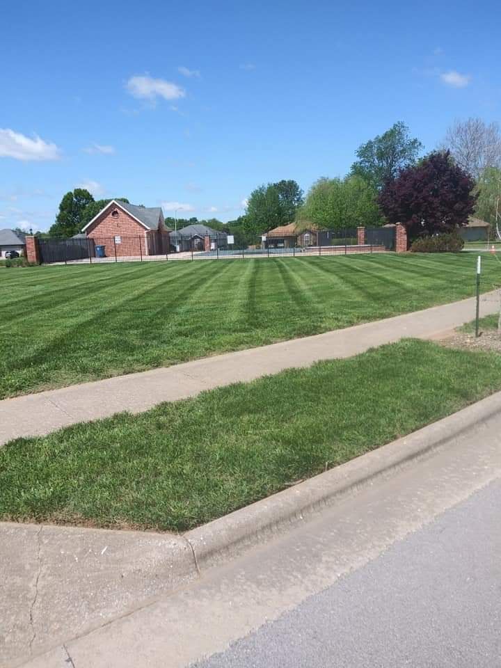 Lawn with alternating stripes, sidewalk in foreground. Red brick house in the background. Bright sunny day.