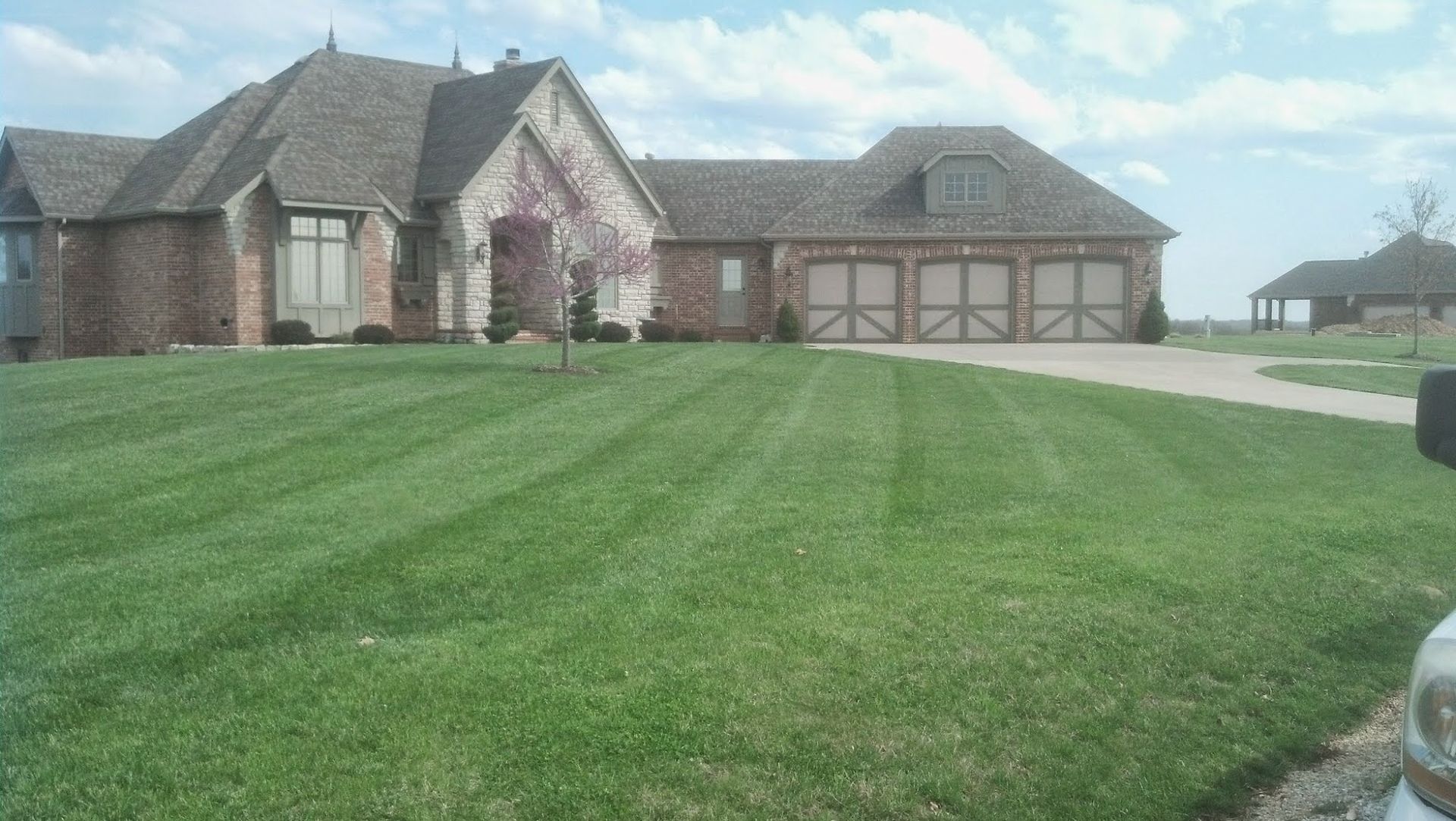 Large brick house with striped green lawn and attached garage. Clear, sunny day.