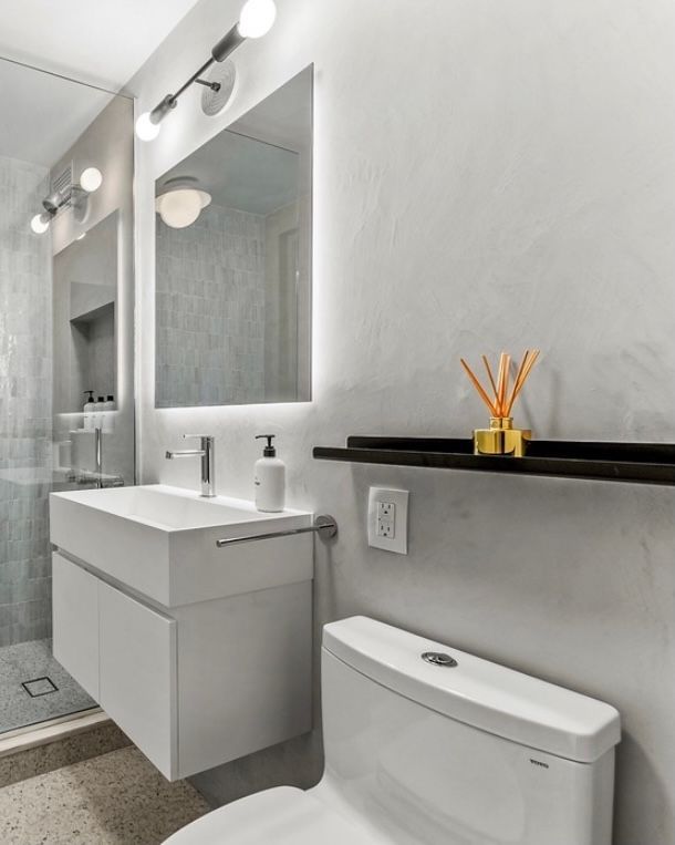 Modern bathroom with white vanity, mirror, toilet, and black shelf with reed diffuser