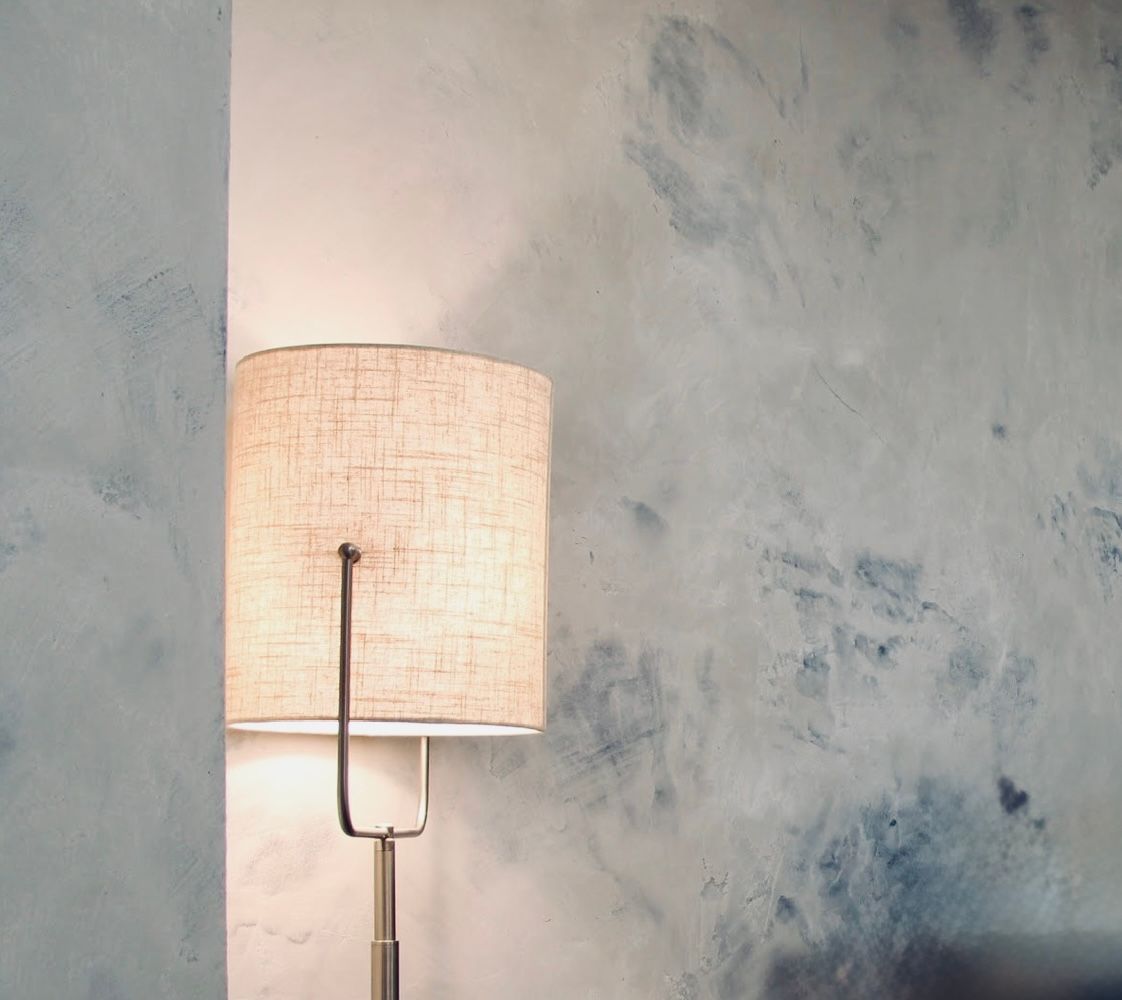 White floor lamp beside a textured gray wall in a softly lit room