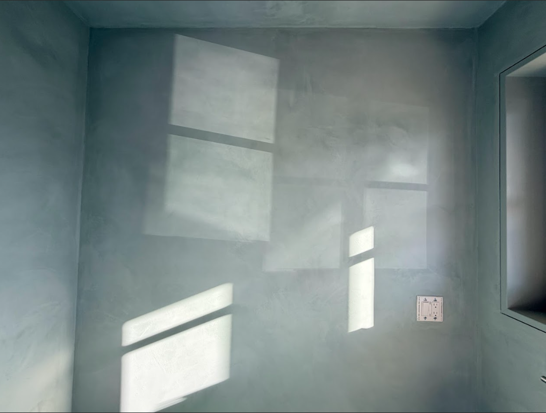 Empty gray room with sunlight rectangles on the walls and a small outlet on the right
