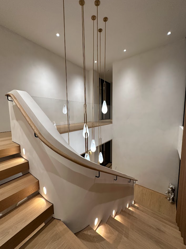 Curved staircase with wooden steps, white walls, and hanging pendant lights in a modern interior