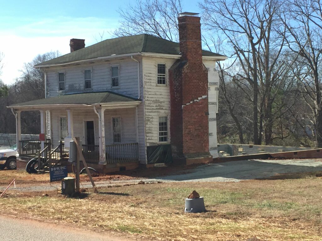 A white house with a brick chimney is being remodeled.