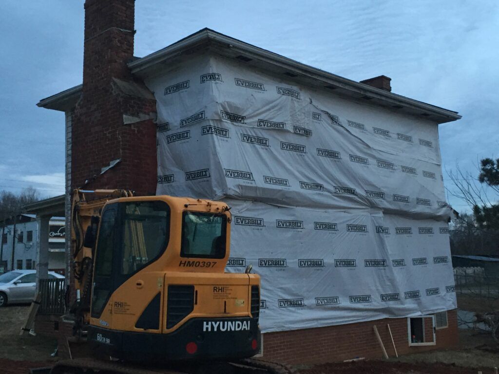 A yellow hyundai excavator is parked in front of a brick building.