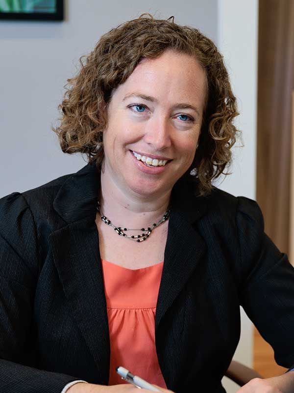 A woman with curly hair is smiling and holding a pen