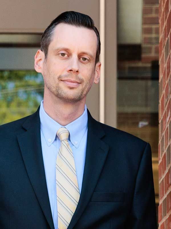 A man in a suit and tie is standing in front of a brick building.