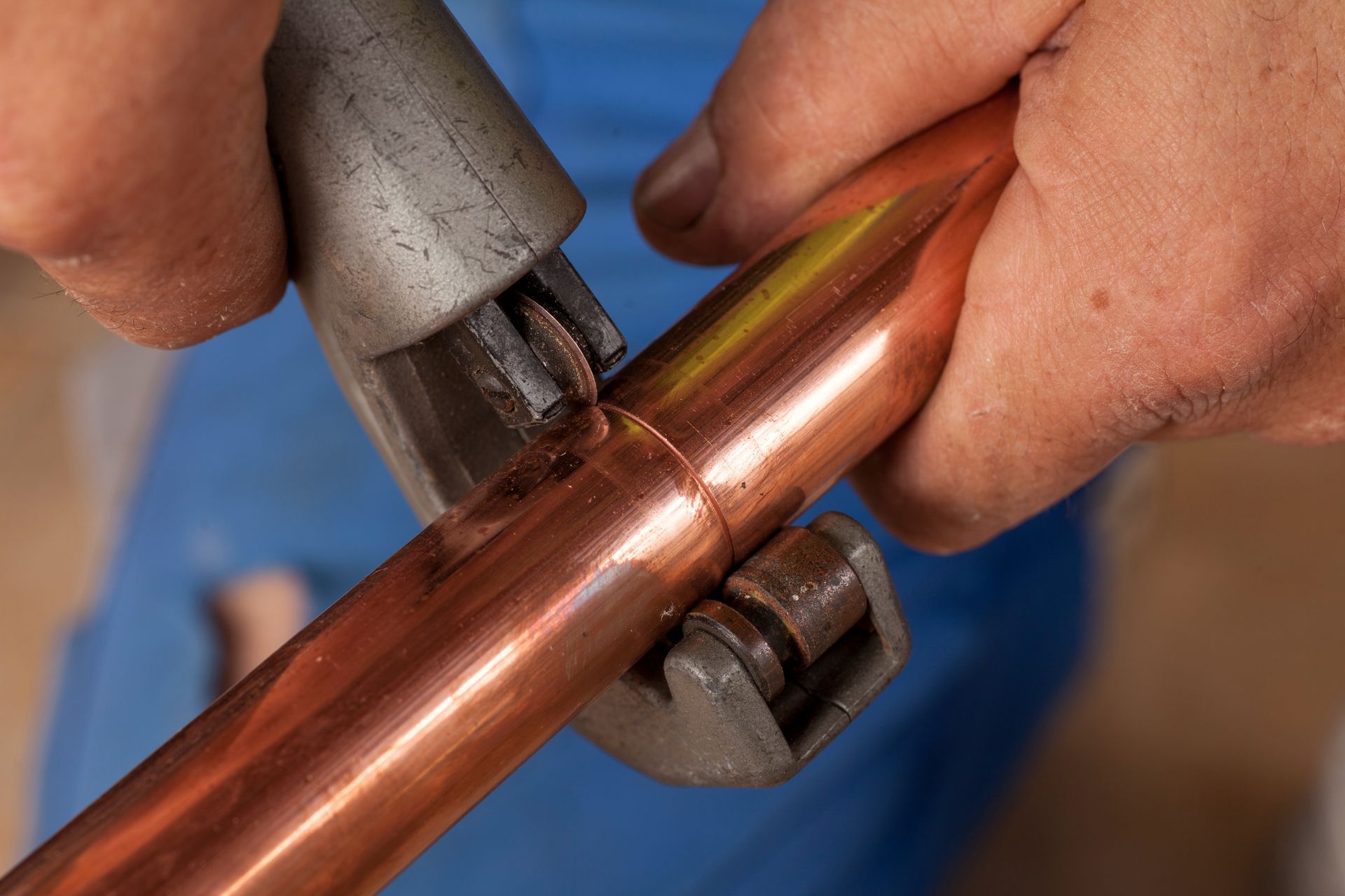 A man is cutting a copper pipe with a pipe cutter.