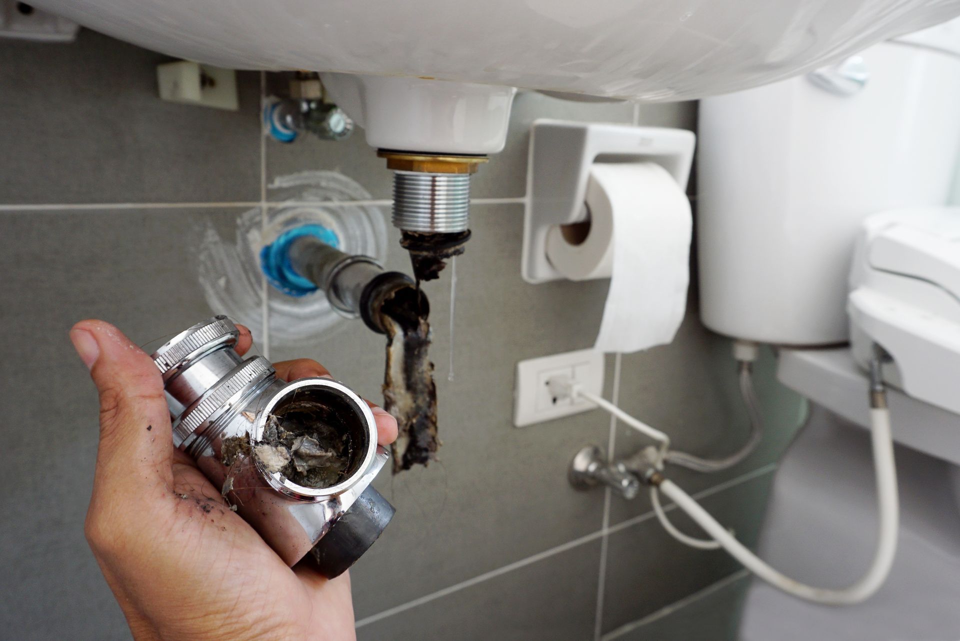 A person is holding a pipe under a sink in a bathroom.