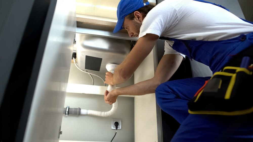 A plumber is fixing a sink in a kitchen.