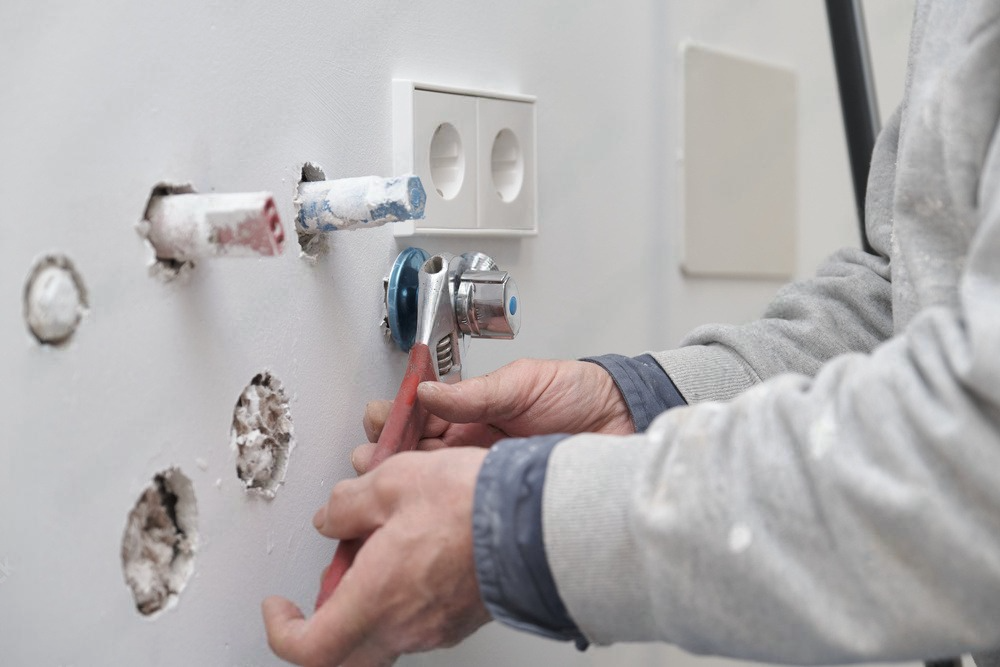 A man is fixing a faucet on a wall with a wrench.