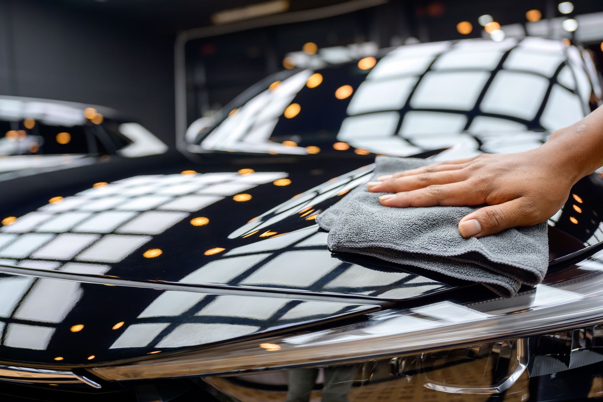Hand wiping a dark car hood with a gray microfiber cloth. Shiny reflections are visible.