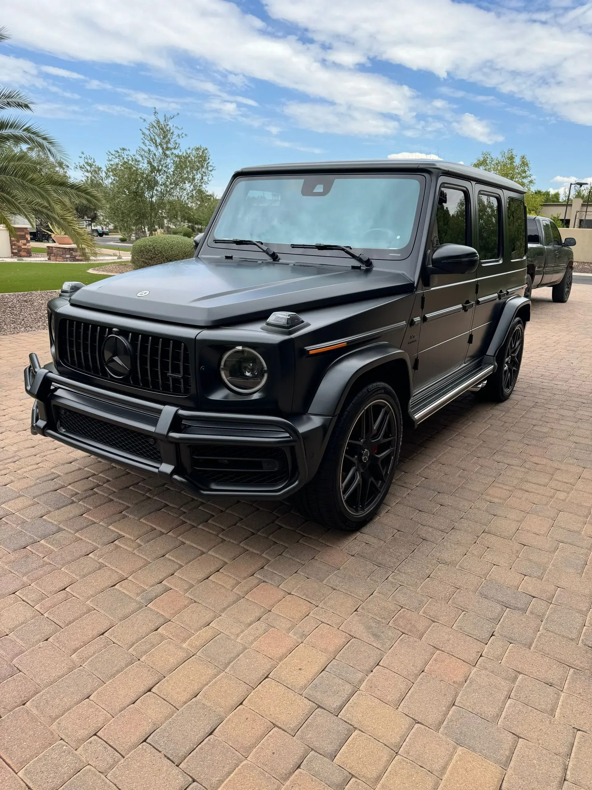 Black Mercedes-Benz G-Wagon SUV parked on a brick driveway, with a dark grille and black rims.