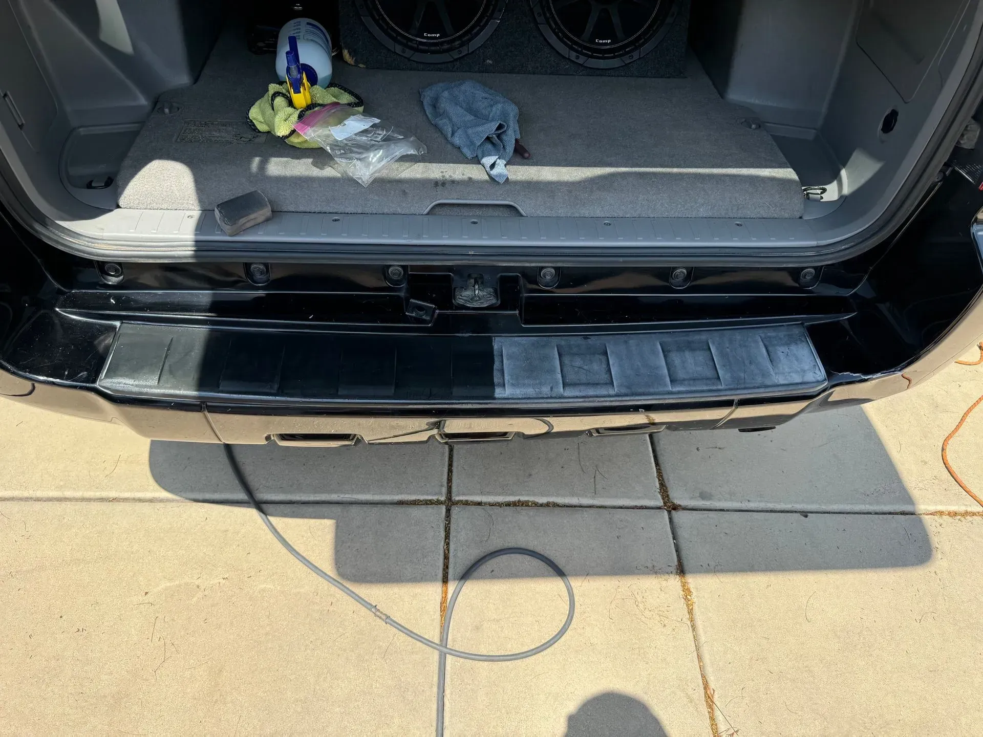 Rear bumper of a black vehicle, half faded, showing restoration progress on a sunny day.