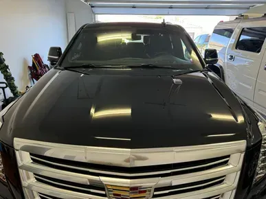 Black Cadillac SUV in a garage, shiny hood reflecting overhead lights.