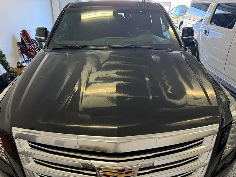 Black Cadillac Escalade SUV parked in a garage, hood reflecting light.
