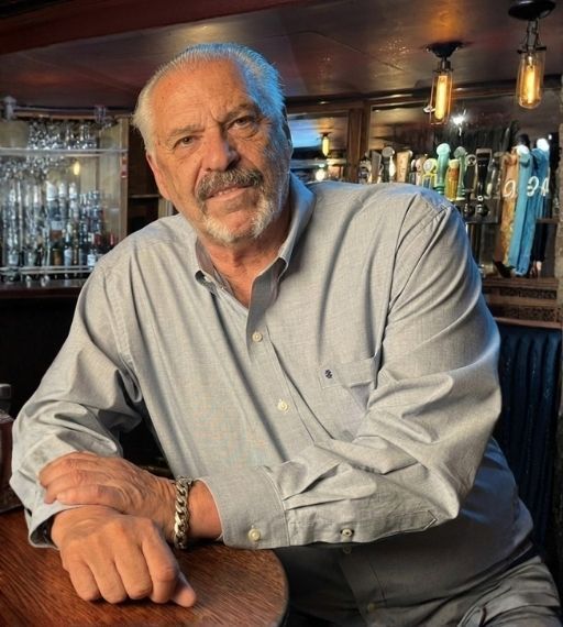 Man smiling, holding up encased cards. Black shirt, gray hair and mustache, cards visible.