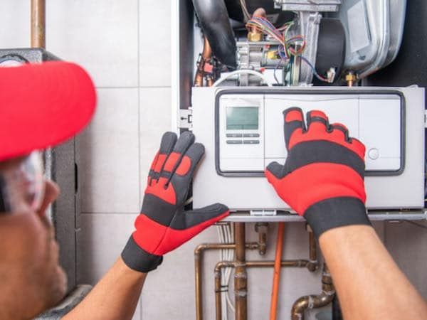 A man wearing red and black gloves is working on a boiler.