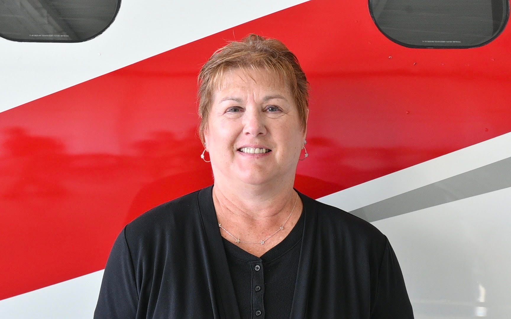A woman in a black shirt is smiling in front of a red and white wall.