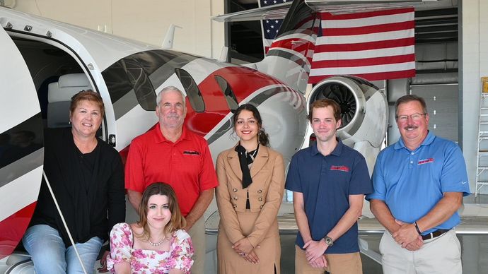 A group of people are posing for a picture in front of an airplane.