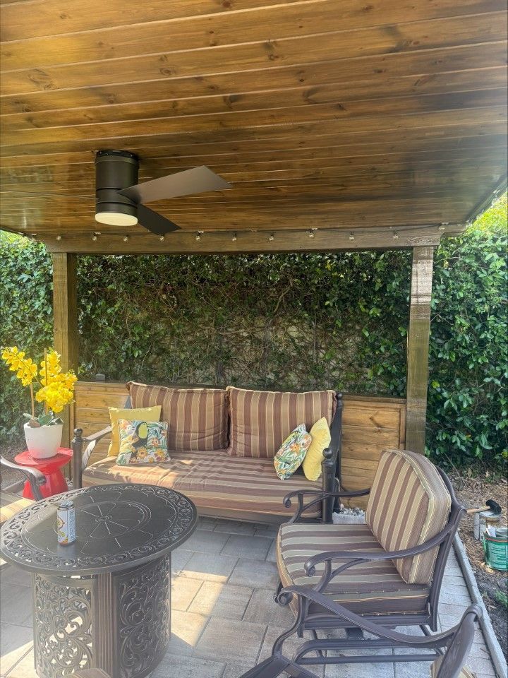 A gazebo with a couch , chairs , a table and a ceiling fan.