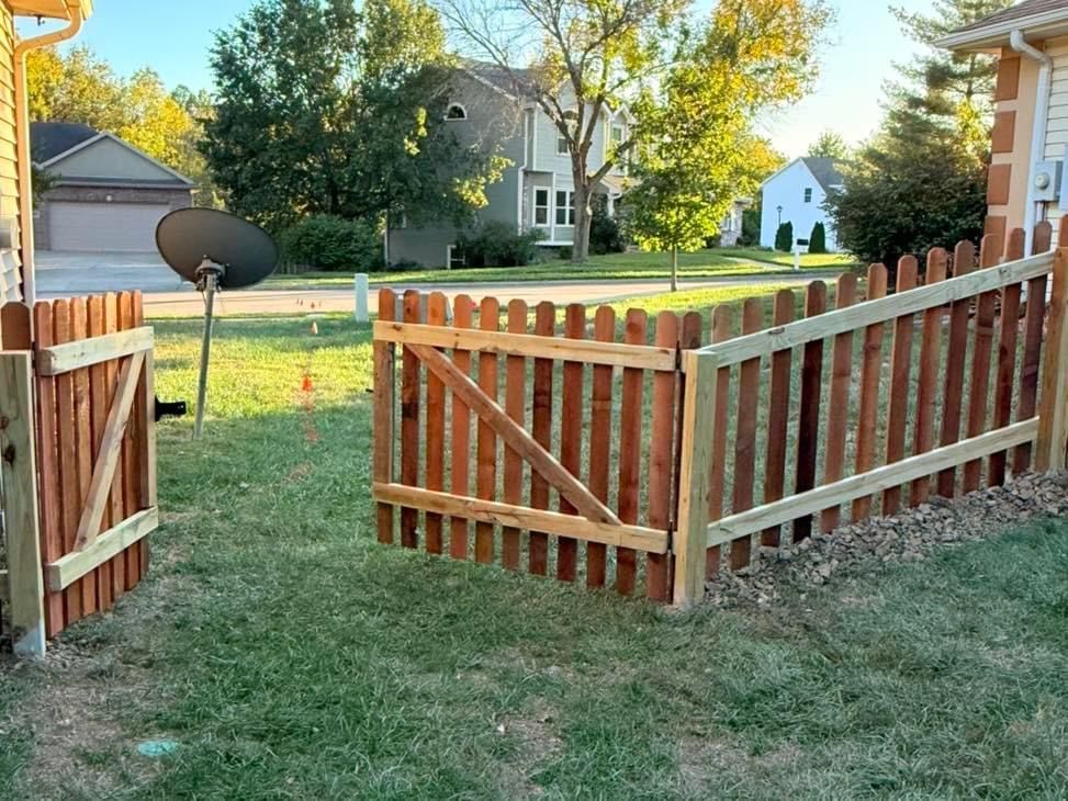A wooden fence is in the middle of a lush green yard.