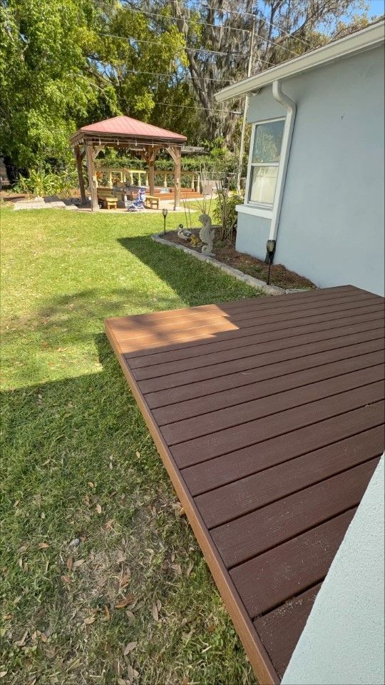 A wooden deck in the backyard of a house with a gazebo in the background.