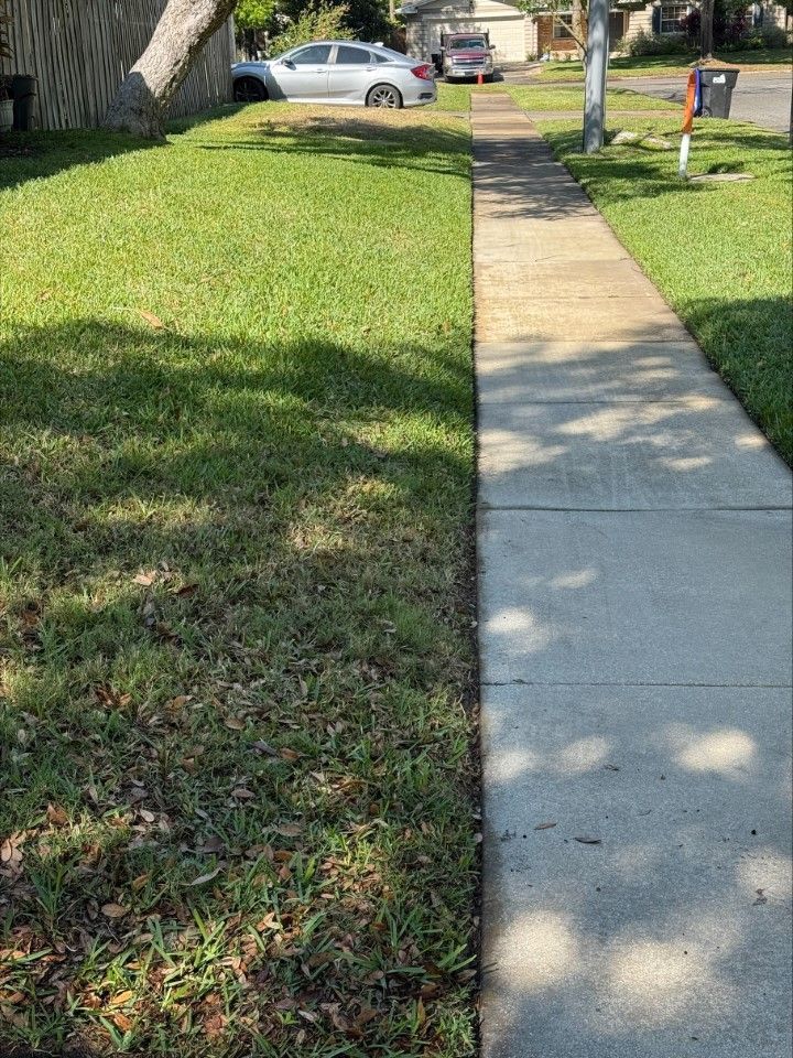 A sidewalk next to a lush green lawn with a car parked in the background.