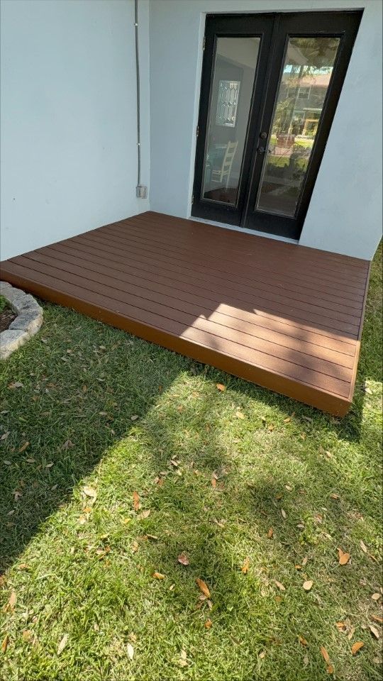 A wooden deck is sitting on top of a lush green lawn in front of a house.