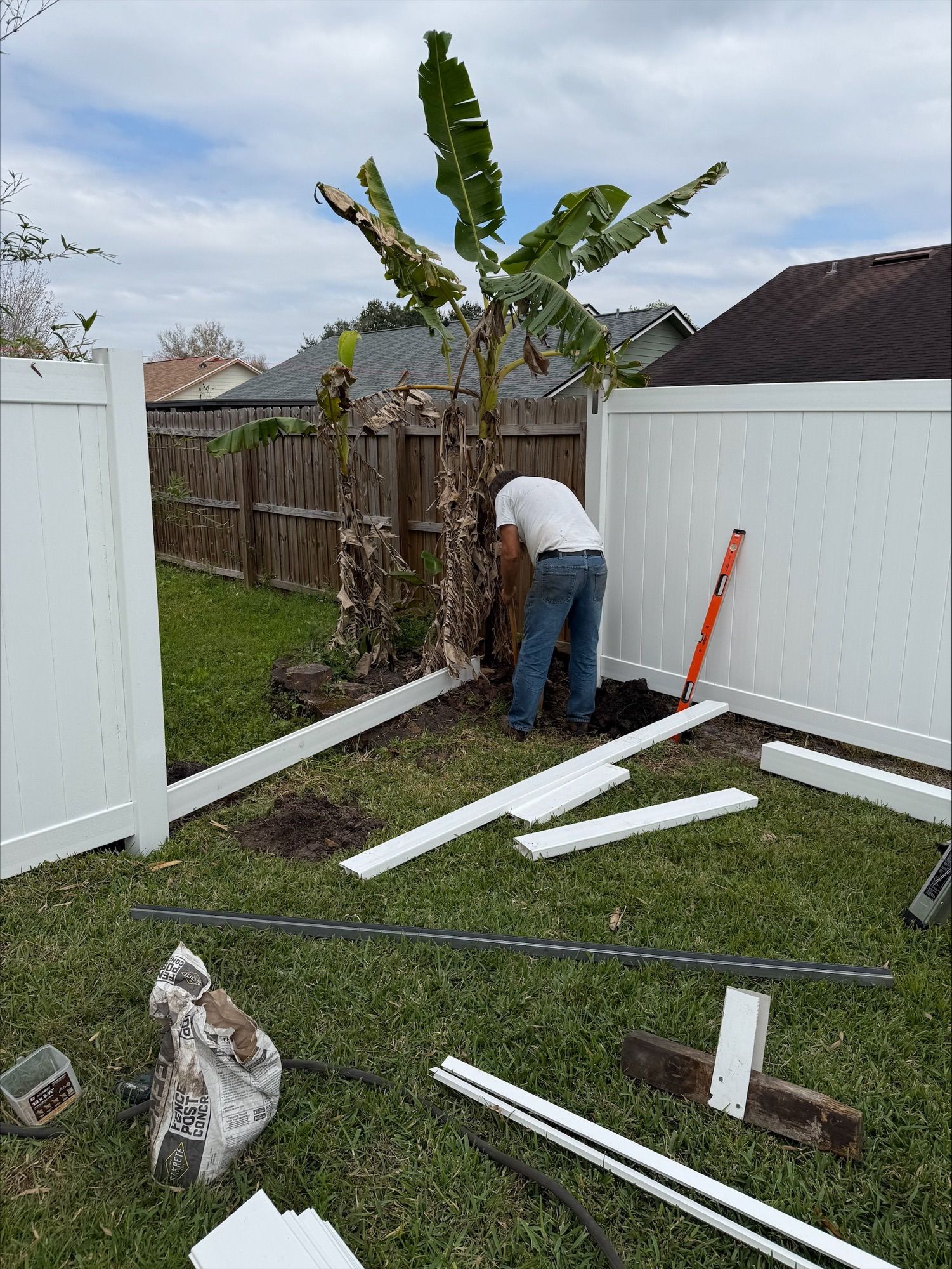 A man is working on a white fence in a backyard.