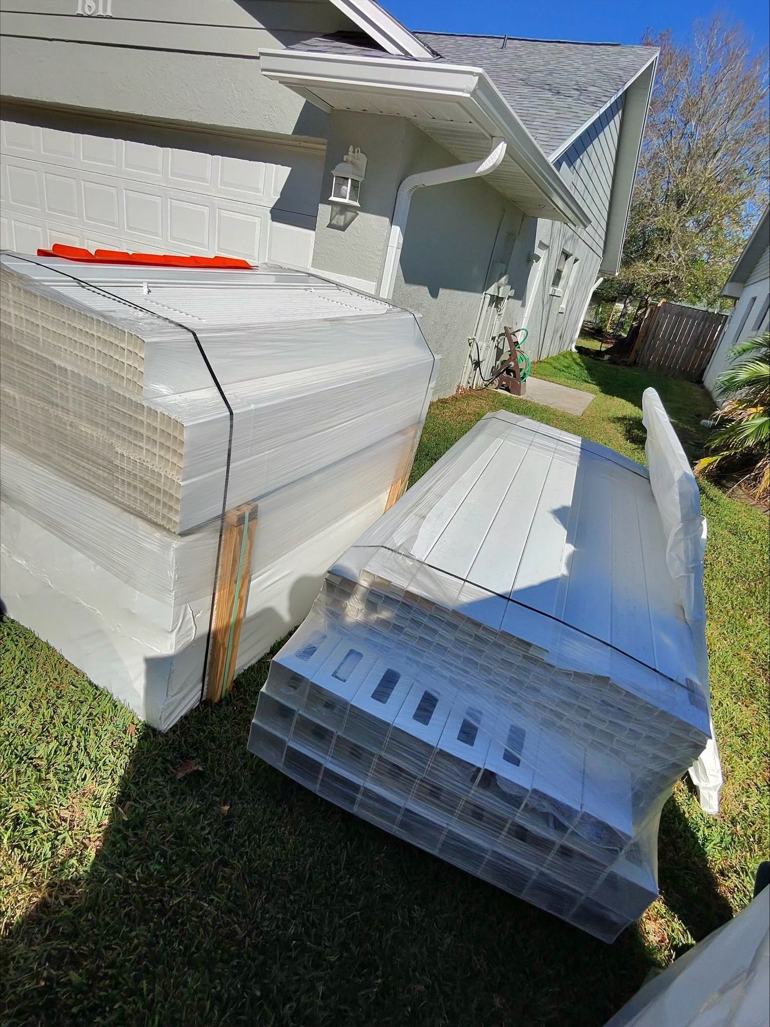 A stack of plastic boxes are sitting on the grass in front of a house.