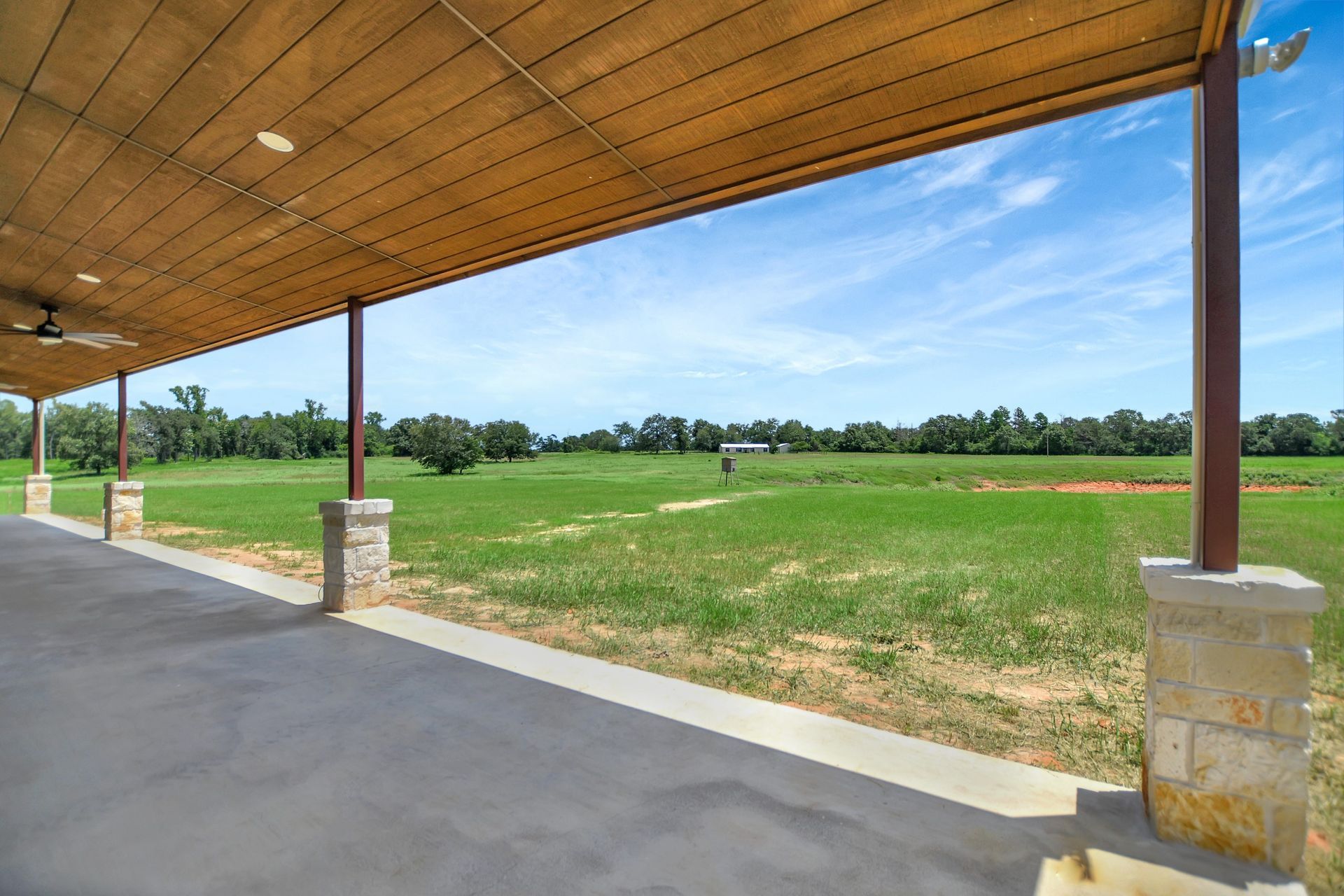 A covered patio overlooks a grassy field under a blue sky.