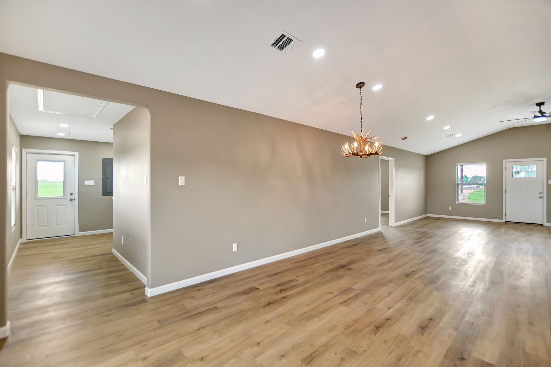 Open-concept living space with wood floors, tan walls, and a chandelier; doors lead to other rooms.