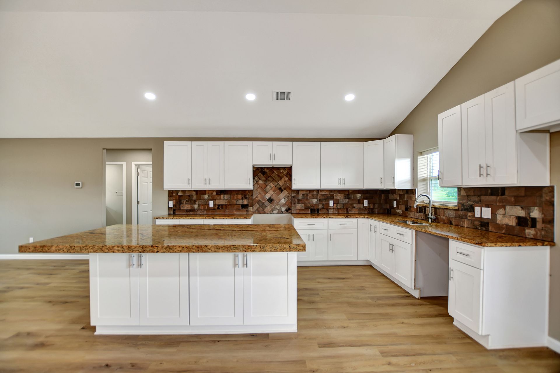 White kitchen with granite countertops and a brown and tan backsplash.