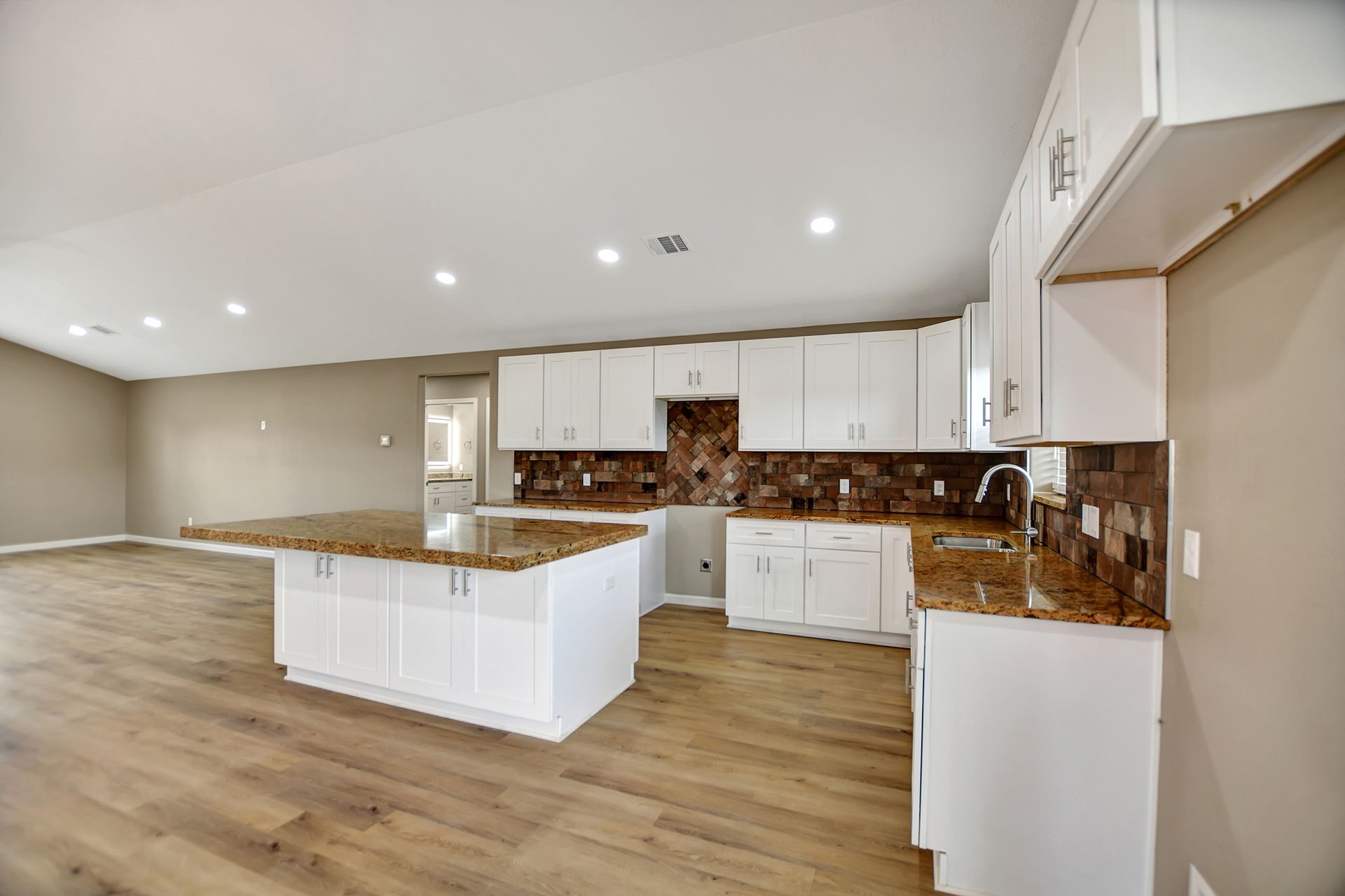 Open kitchen with white cabinets, island, granite counters, wood-look floors, and neutral walls.